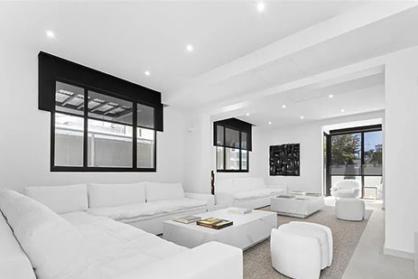 Modern living room renovation by ACJ General Contractor featuring all-white interior, black-framed windows, recessed lighting and natural light.
