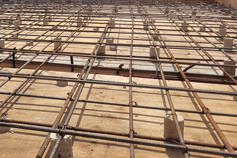 Roof slab under construction with structural steel reinforcement mesh laid on wooden formwork and grid of steel rebars.