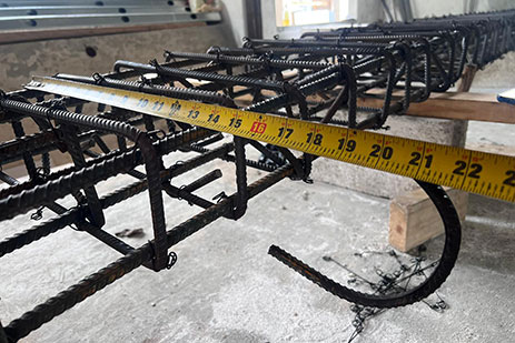 Close-up view of steel reinforcement for concrete structure with yellow measuring tape stretched across.