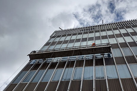 Workers on swing stage, cleaning and maintaining exterior windows of high-rise office building.
